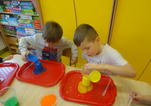 Dwóch chłopców dolewa zabarwioną ciecz do swoich słoiczków.